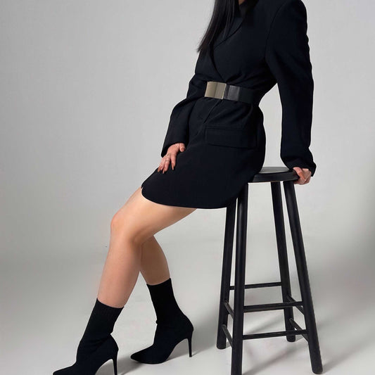 femme assise sur un tabouret portant un blazer noir porté en robe avec une ceinture